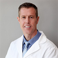 Image of Brian Loveridge in white lab coat, blue shirt, and blue tie.