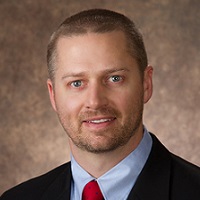 Image of Clinical Services Supervisor wearing a black jacket, blueshirt, and red tie.